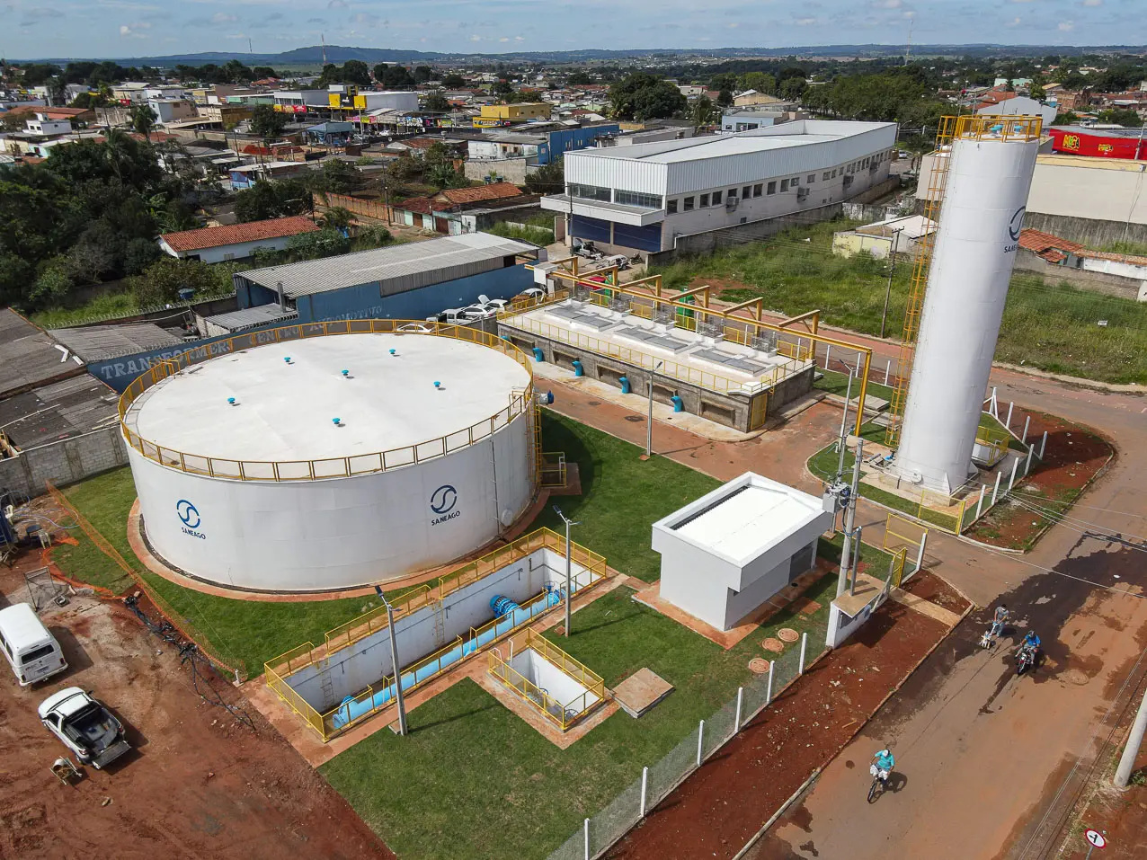 A imagem mostra uma estação de tratamento de água da Saneago em Aparecida de Goiânia. O local possui grandes reservatórios, estruturas técnicas e áreas verdes, cercado por um bairro urbano com comércios e residências ao fundo.