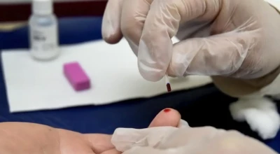 Profissional da saúde coleta uma gota de sangue da ponta do dedo de um paciente durante teste rápido, em cenário típico de triagem para hepatites virais.