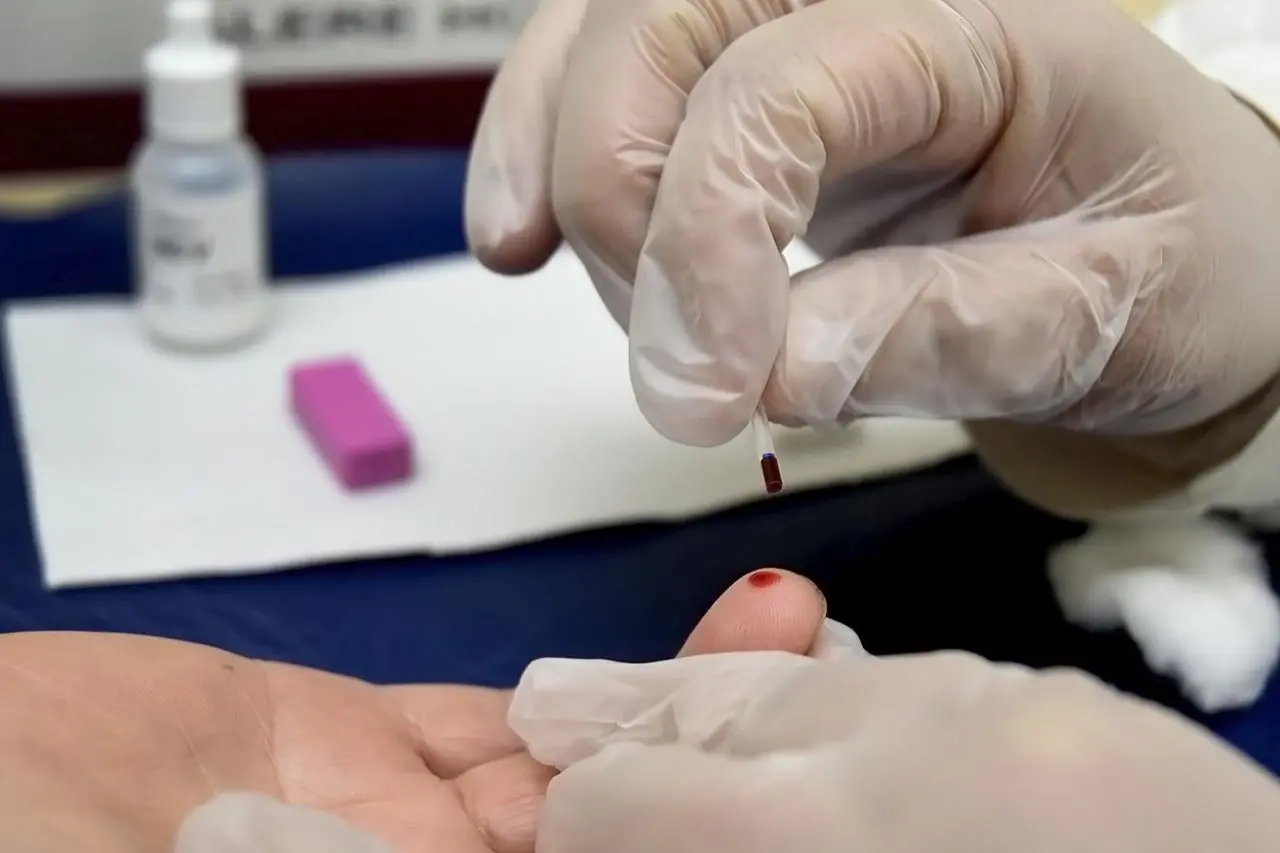 Profissional da saúde coleta uma gota de sangue da ponta do dedo de um paciente durante teste rápido, em cenário típico de triagem para hepatites virais.