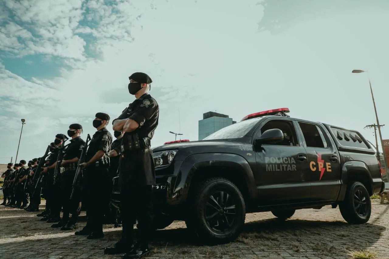 Policiais da CPE estão perfilados ao lado de uma viatura