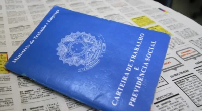 Carteira de Trabalho azul sobre classificados de jornal simboliza a busca por emprego e a formalização profissional.