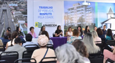 Imagem mostra a mesa diretiva da 3ª Conferência de Políticas para Mulheres de Aparecida, com representantes debatendo propostas e direitos.