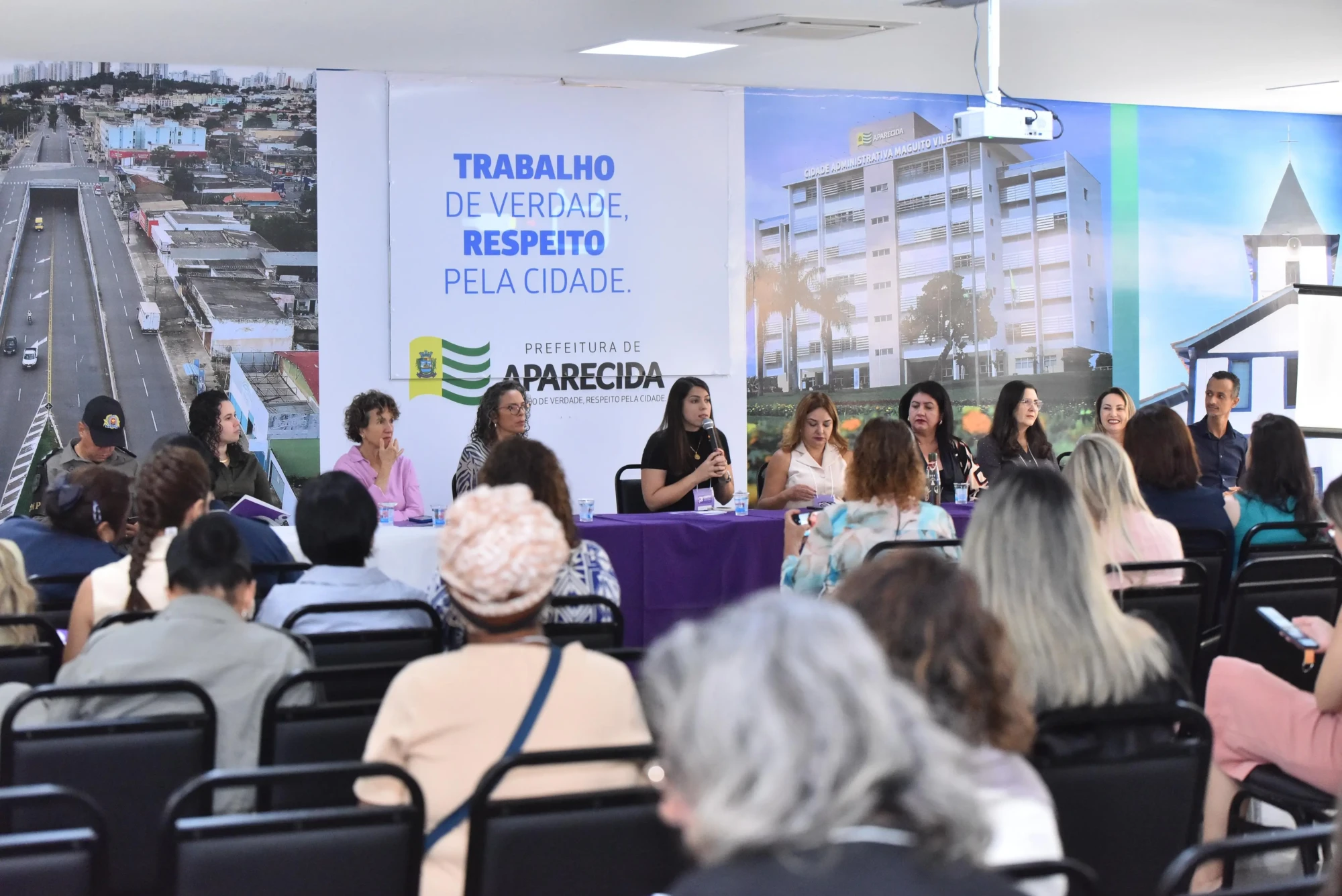 Imagem mostra a mesa diretiva da 3ª Conferência de Políticas para Mulheres de Aparecida, com representantes debatendo propostas e direitos.