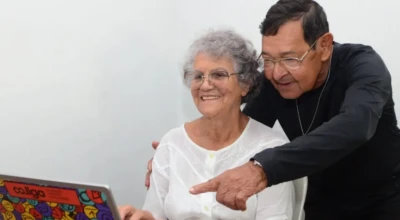 Idosos interagem com um notebook, sorrindo enquanto exploram juntos a tecnologia