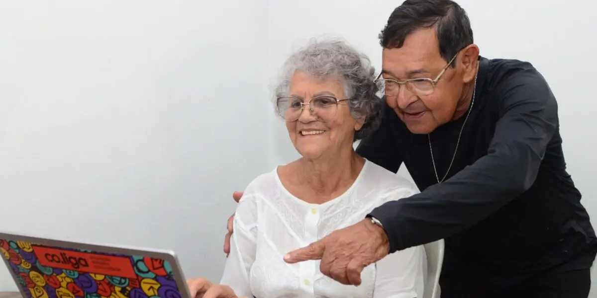 Idosos interagem com um notebook, sorrindo enquanto exploram juntos a tecnologia