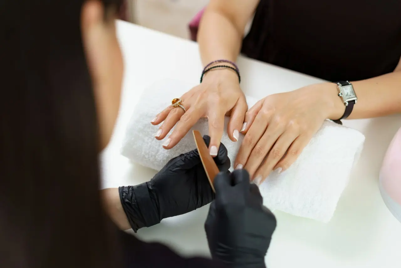 Profissional faz o lixamento das unhas de uma mulher em atendimento de manicure