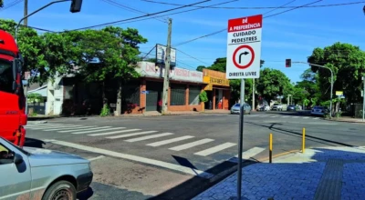 A imagem mostra um cruzamento urbano sinalizado, com faixa de pedestres e placa indicando “Dê a preferência – Cuidado pedestres – Direita livre”.
