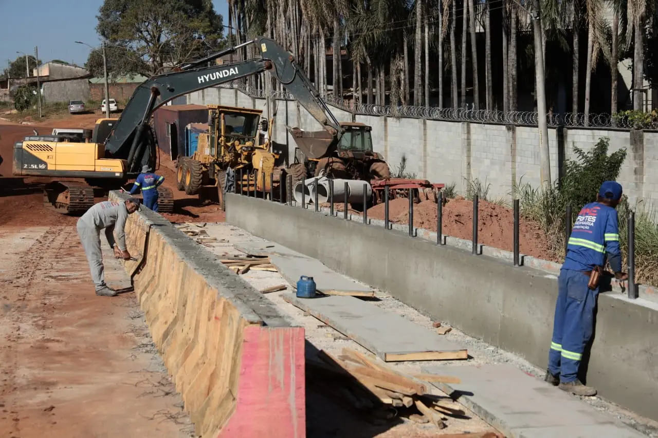 Trabalhadores atuam na construção de uma galeria de concreto, com uso de escavadeiras e tratores, em obra de drenagem em área urbana.