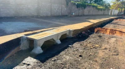 Trecho de rua em obra com nova galeria de drenagem em concreto e calçada concluída, aguardando aplicação da camada de asfalto.