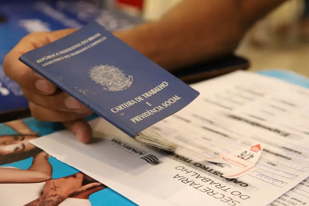 Carteira de Trabalho e Previdência Social azul sobre uma mesa com formulários e ficha de atendimento.