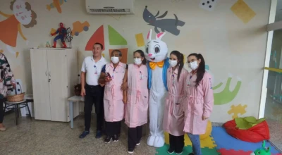 Voluntários do HMAP posam ao lado de um coelho da Páscoa em atividade lúdica na brinquedoteca do hospital.