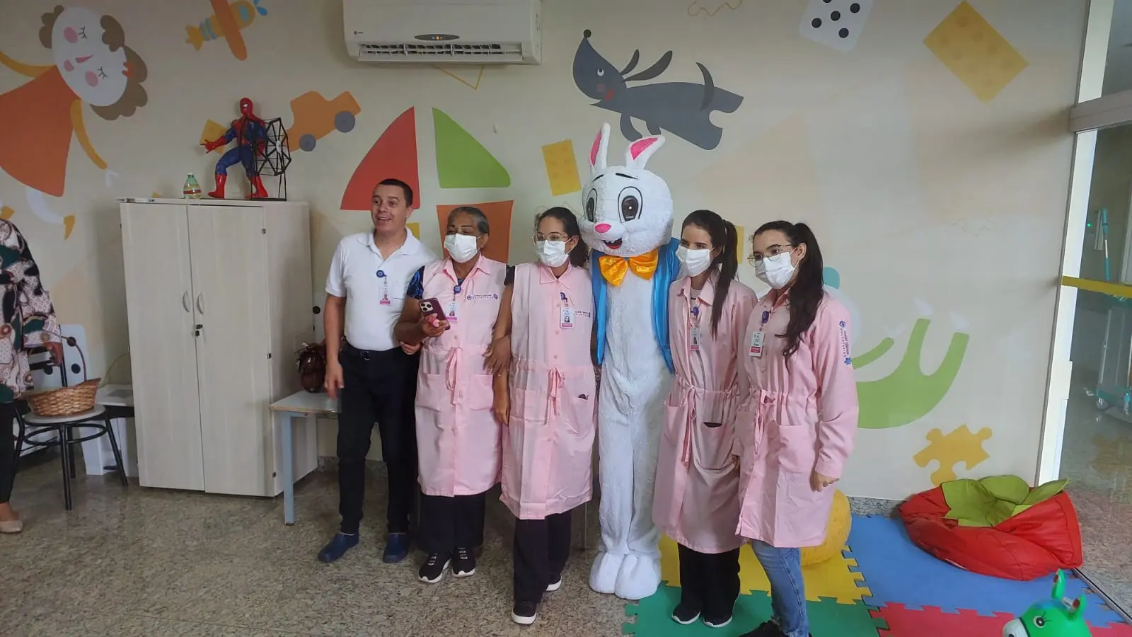 Voluntários do HMAP posam ao lado de um coelho da Páscoa em atividade lúdica na brinquedoteca do hospital.