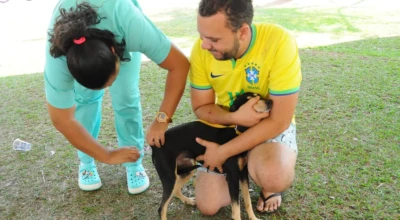 Profissional de saúde aplica vacina em um cão, enquanto o tutor segura o animal.
