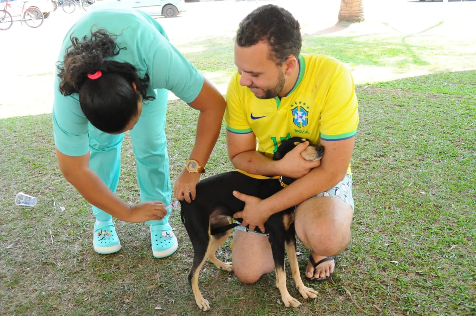 Profissional de saúde aplica vacina em um cão, enquanto o tutor segura o animal.