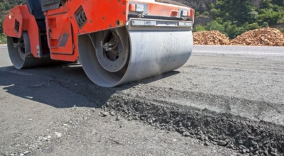 Máquina laranja compacta asfalto recém-aplicado em obra de recapeamento.
