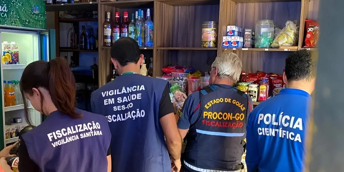 Equipe de fiscalização dentro de um comércio de Aparecida, conferindo prateleiras com bebidas e alimentos. *