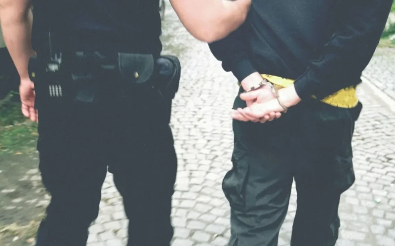 Foto de policial com suspeito algemado.