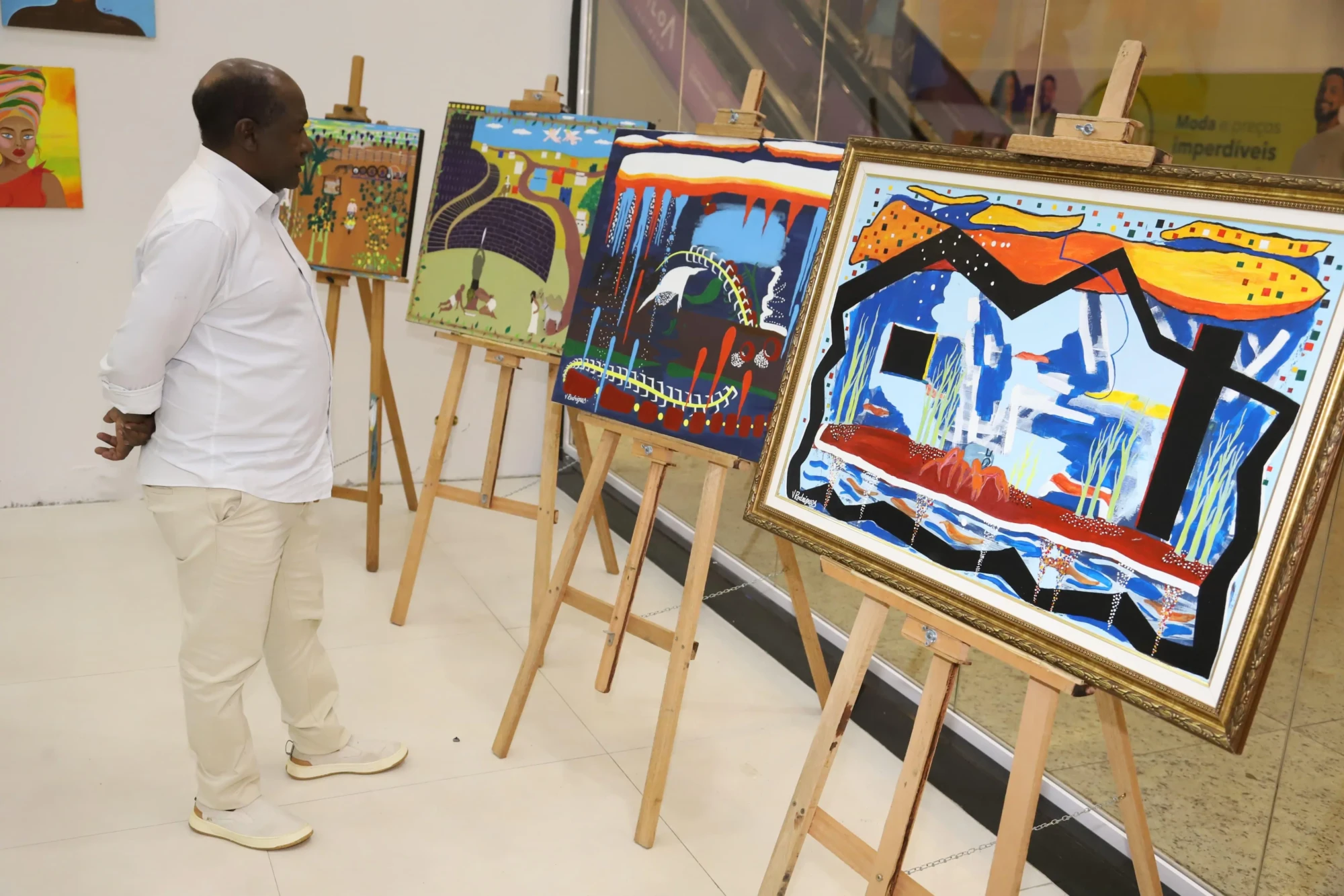 Foto de um homem admirando artes expostas em um salão.