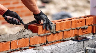Pedreiro levantando muro em obra.