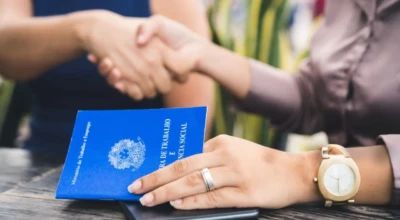 Pessoas apertando as mãos e na mesa uma carteira de trabalho