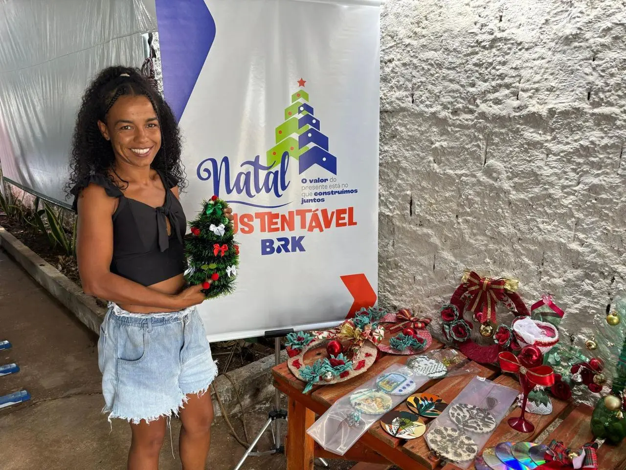 Participante do projeto natal sustentável ao lado dos itens produzidos com reciclagem.