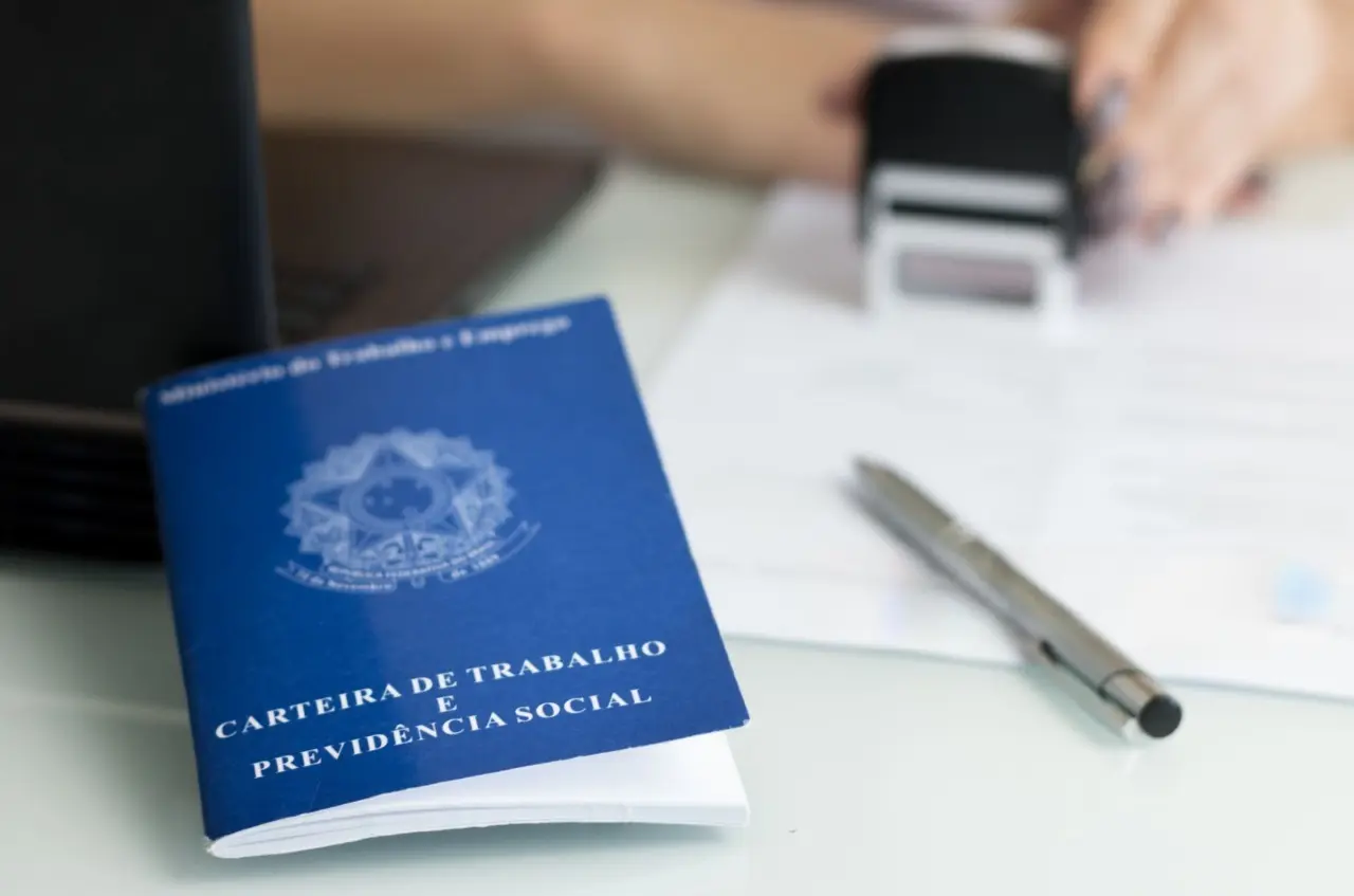 Carteira de trabalho em cima de uma mesa com uma caneta e carimbo.